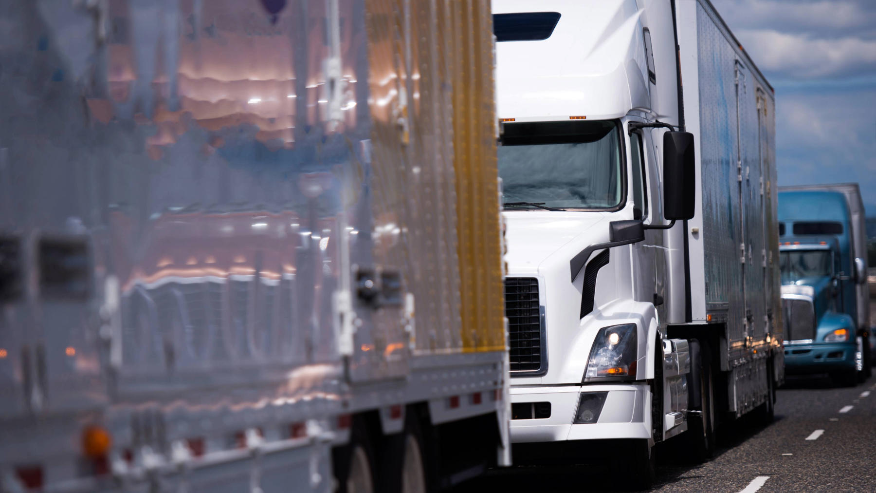 A line of semi-trucks driving on a highway, maintaining safe speed and distance. Proper speed and space management are key for truck drivers to improve safety and efficiency on the road.