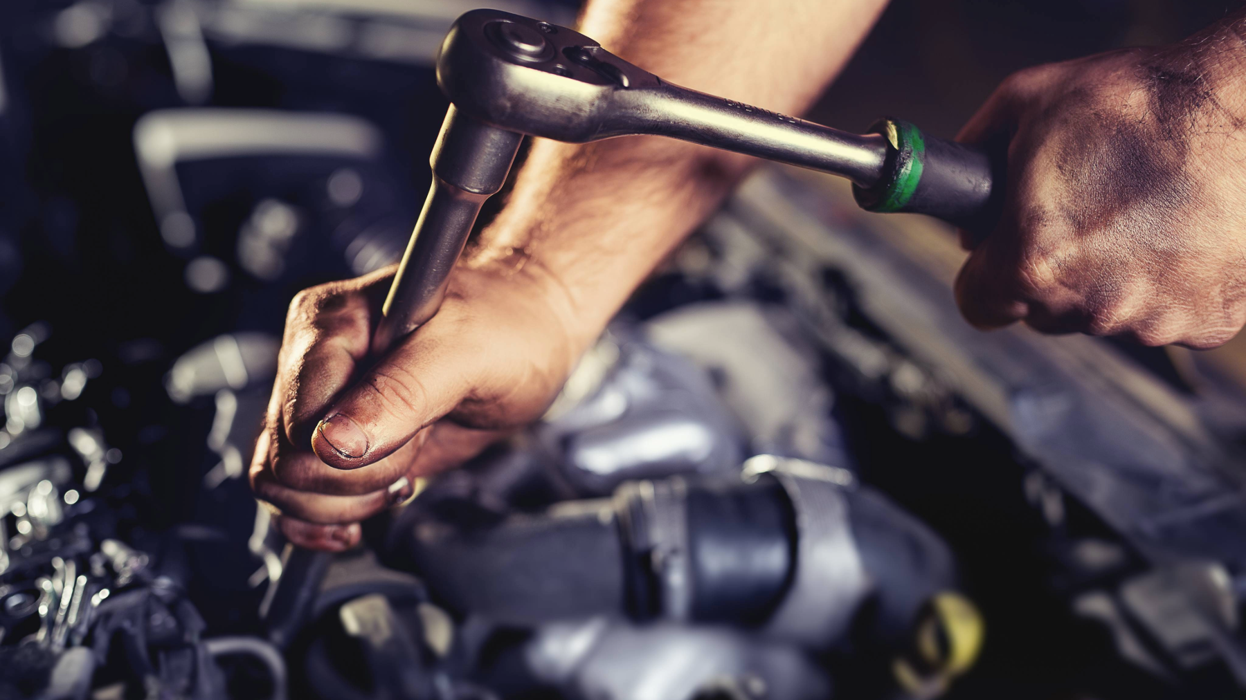 Close-up of a diesel technician’s hands using a ratchet wrench to tighten a bolt under the hood. Having the right diesel technician tools is essential for efficiency, precision, and quality repairs.