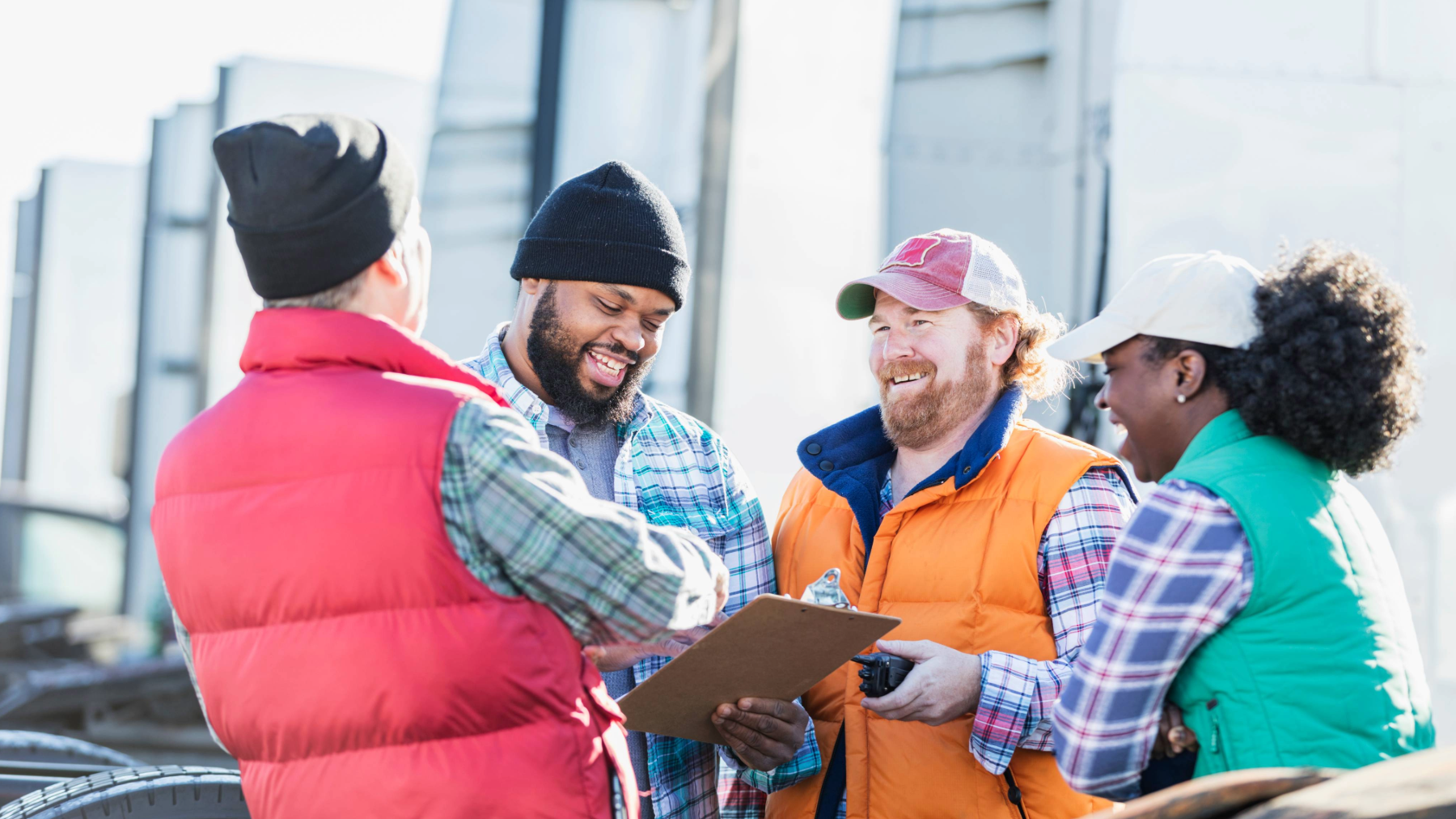 Truck drivers and their manager sharing a conversation and reviewing paperwork together in a trucking yard, emphasizing teamwork, communication tips, and collaboration in the transportation industry.