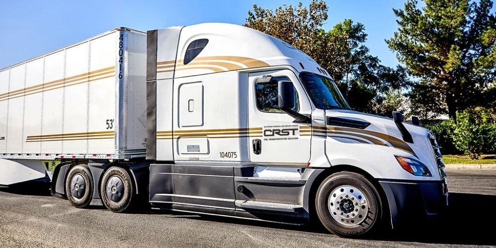 CRST semi-truck with a 53-foot trailer parked on a sunny road, featuring the company's logo and gold-striped branding.